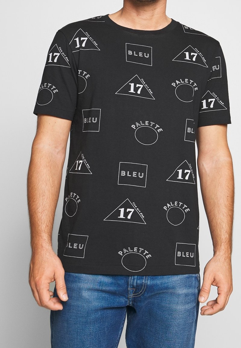 Camiseta de algodón negra con diversas formas geométricas blancas y gráficos de texto, incluyendo "BLEU" y "17", con mangas cortas y cuello redondo.