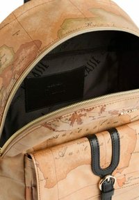Ingrandimento di uno zaino beige aperto con una stampa di mappa del mondo, che mostra una tasca anteriore con una tracolla nera e una fibbia dorata.