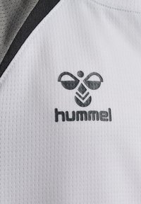 Logo d'abeille hummel noir et gris imprimé sur un tissu sportif blanc texturé avec des panneaux gris et noirs dans le coin supérieur.