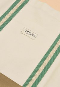 Borsa tote in tela con base color cuoio e parte superiore color crema. Presenta spallacci intrecciati verdi e crema, e una targhetta Joules ben visibile.