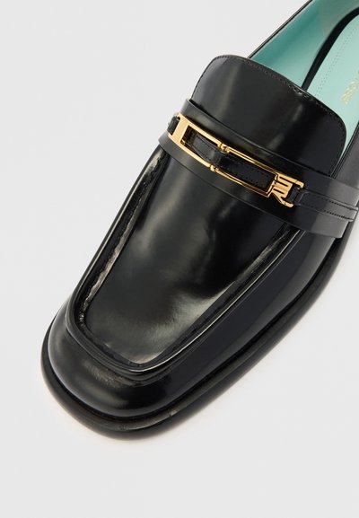 Czarny skórzany loafers z błyszczącym wykończeniem, z złotym metalowym akcentem na pasku i zaokrąglonym czubkiem.