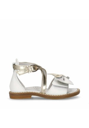 Witte leren sandaal met gouden accenten, met een strikdetail, verstelbare enkelband en een platte, bruine rubberen zool.