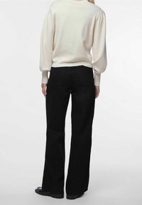 Pantalones negros de pierna ancha hechos de un tejido texturizado, con una cintura alta y dos bolsillos traseros, acompañados de un suéter crema con mangas abullonadas.