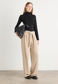 Crni rolak, bež hlače s visokim strukom i nabranim detaljima s tkanim remenom, te velika crna kožna torba. Sjajne crne cipele.