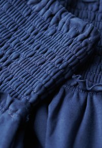 Tela azul marino con textura fruncida, que presenta secciones recogidas y una textura suave. Enfoque cercano en detalles elásticos y costuras.