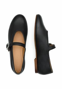 Bailarinas de piel negra con un detalle de hebilla circular plateada en la correa y un tacón bajo marrón. Textura suave con punta redondeada.