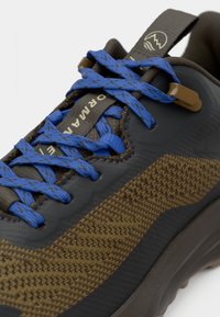 Nahaufnahme eines braunen und schwarzen Sneakers mit blauen, gemusterten Schnürsenkeln und einer Zuglasche mit einem Berglogo.
