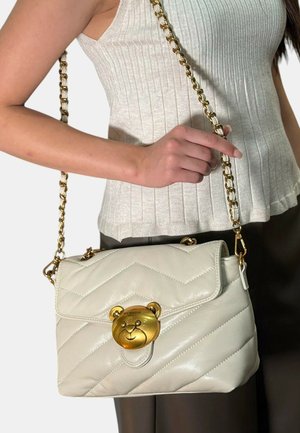 Borsa a mano in pelle bianca trapuntata con clasp a forma di orso dorato, tracolla a catena e chiusura a patta. Decorata con un motivo testurizzato.
