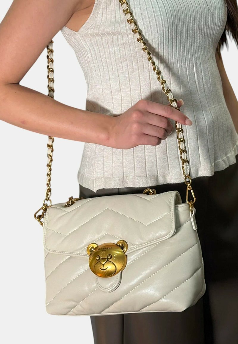Borsa a mano in pelle bianca trapuntata con clasp a forma di orso dorato, tracolla a catena e chiusura a patta. Decorata con un motivo testurizzato.