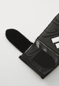 Black leather glove with textured surface; features a Velcro closure and white logo accents. Smooth inner lining and reinforced stitching.
