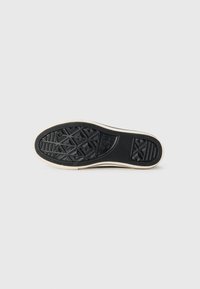 Semelle de chaussure en caoutchouc noir avec un motif de grip texturé et des bords latéraux de couleur crème. Comprend des motifs géométriques et une empreinte de logo.