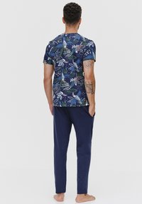 Granatowy zestaw piżamowy z tropikalnym wzorem na bluzce z krótkimi rękawami oraz gładkich granatowych spodniach. Miękka tkanina, luźny krój i długość do kostek.