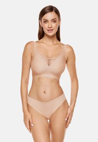 Beżowy biustonosz typu bralette z siateczkowym panelem w kształcie litery V z przodu, szerokimi ramiączkami i gładkim materiałem. Dopasowane gładkie figi bikini.