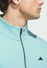 Sudadera azul claro de forro polar con media cremallera y cuello alzado, que presenta una cremallera negra y un pequeño logo triangular negro en el pecho.