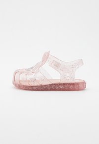 Sandalia de gel rosa clara con destellos, diseño abierto que presenta recortes, correa ajustable y plantilla suave. Punta redondeada y suela plana.