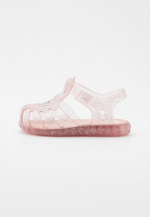 Sandalia de gel rosa clara con destellos, diseño abierto que presenta recortes, correa ajustable y plantilla suave. Punta redondeada y suela plana.