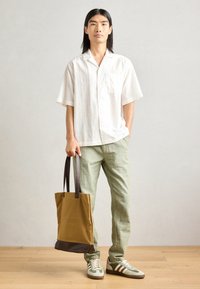 White short-sleeve shirt, light green linen pants, green-and-beige sneakers with white stripes, brown-bottomed tote bag with dark handles.