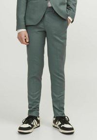 Pantaloni in grigio chiaro su misura realizzati in tessuto morbido, dalla forma aderente, con tasche incluse, abbinati a sneaker bianche e nere.