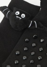 Czarne skarpetki z pluszową postacią nietoperza na górze, z dwoma dużymi białymi oczami i kłami. Podeszwy mają czarne gumowe kropki dla lepszej przyczepności.