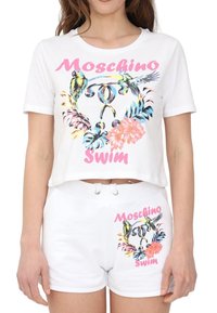 Conjunto de camiseta corta blanca y pantalones cortos con estampados coloridos de loros y flores, con texto "Moschino Swim" en rosa en ambas piezas.