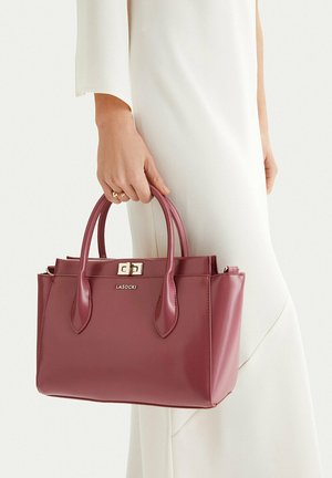 Kobieta w białej sukience trzyma bordową skórzaną torebkę Lasocki z podwójnymi uchwytami i złotym zapięciem.