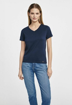 Granatowy t-shirt z dekoltem w serek i krótkimi rękawami, wykonany z bawełny. Charakteryzuje się luźnym krojem i małym logo na dolnym skraju. W zestawie z niebieskimi dżinsami.
