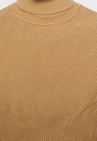 Beiger Rollkragenpullover aus Strickstoff, mit strukturiertem Fischgrätenmuster und tailliertem Schnitt. Weiches, atmungsaktives Material.