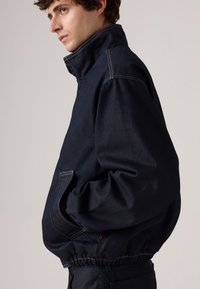 Marineblauwe denimjas met een hoge kraag, elastische tailleband, zijzakken en contrasterende witte stiksels. Ontwerp met een casual pasvorm.