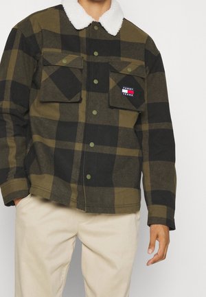 Ternet grøn og sort jakke med en hvid shearling krave, der har to brystlommer og et brandlogo på venstre lomme.