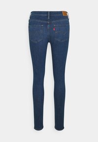 Jeans de mezclilla azul delgados con una cintura de altura media, dos bolsillos traseros y una etiqueta de logo de cuero marrón en la cinturilla. Textura suave.