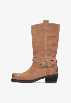 Botte montante en daim de couleur marron clair, avec une sangle à boucle et un bout légèrement arrondi. Talon bas empilé et dessus texturé.