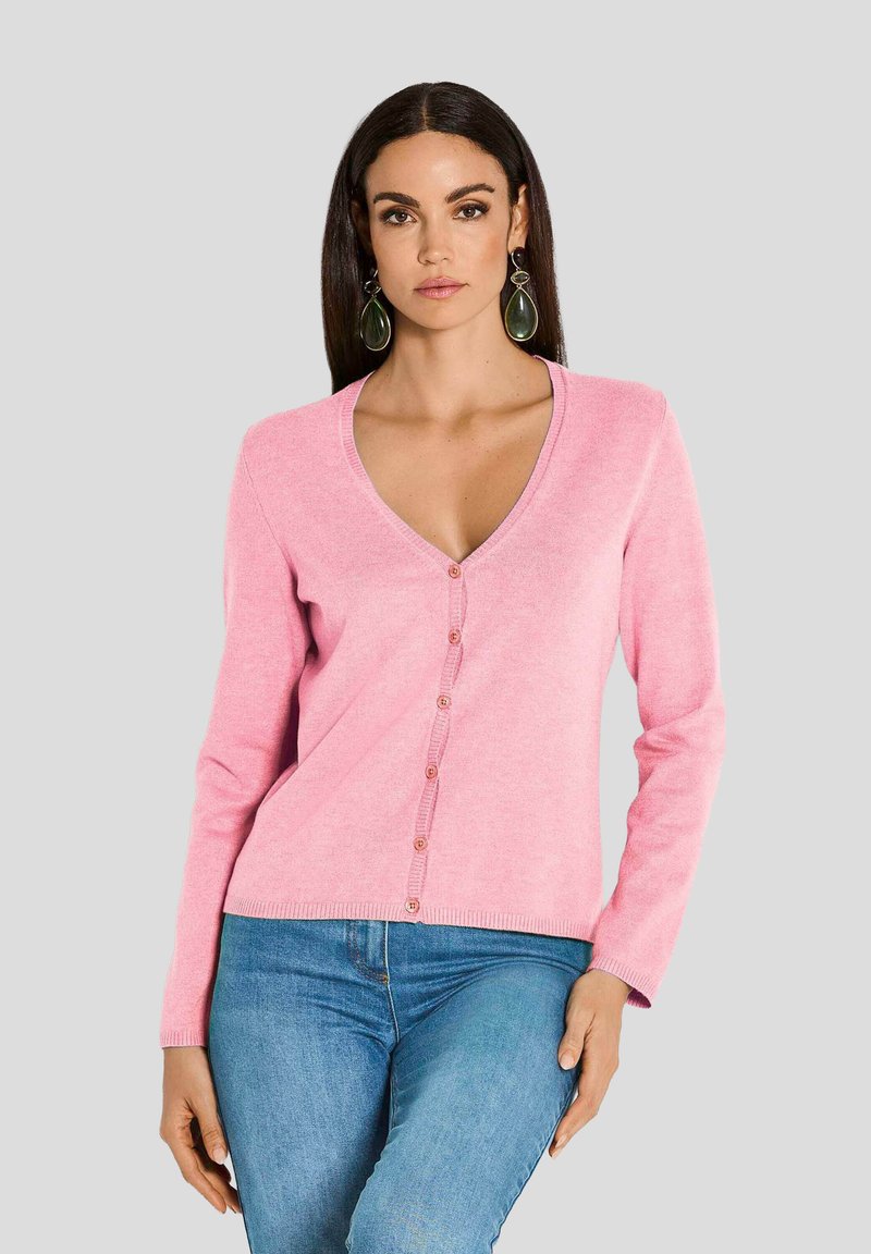 Rosa Strickjacke aus weichem Stoff, mit V-Ausschnitt, langen Ärmeln und durchgehender Knopfleiste mit passenden Knöpfen, kombiniert mit blauen Jeans.