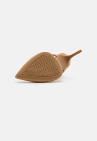 Scarpa con tacco alto e punta affusolata, realizzata in materiale beige liscio. La suola presenta un motivo di grip texturizzato per garantire aderenza.