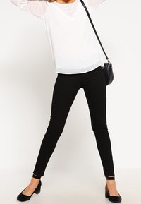 Top bianco a maniche lunghe con scollatura in pizzo, abbinato a leggings neri aderenti e scarpe basse nere. Design semplice, texture liscia e colori a contrasto.