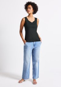 Czarny bezrękawnik z dekoltem w kształcie litery V, w zestawieniu z jasnoniebieskimi spodniami typu wide-leg z przednimi kieszeniami i srebrnymi akcentami.