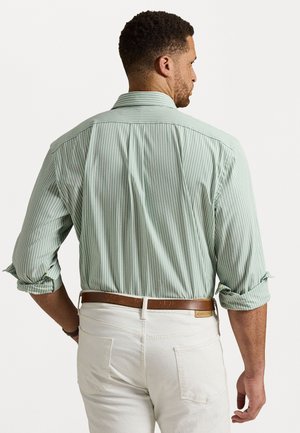 Light green striped shirt with roll-up sleeves, back pleat detail, and a brown belt, paired with white pants. Smooth fabric texture.