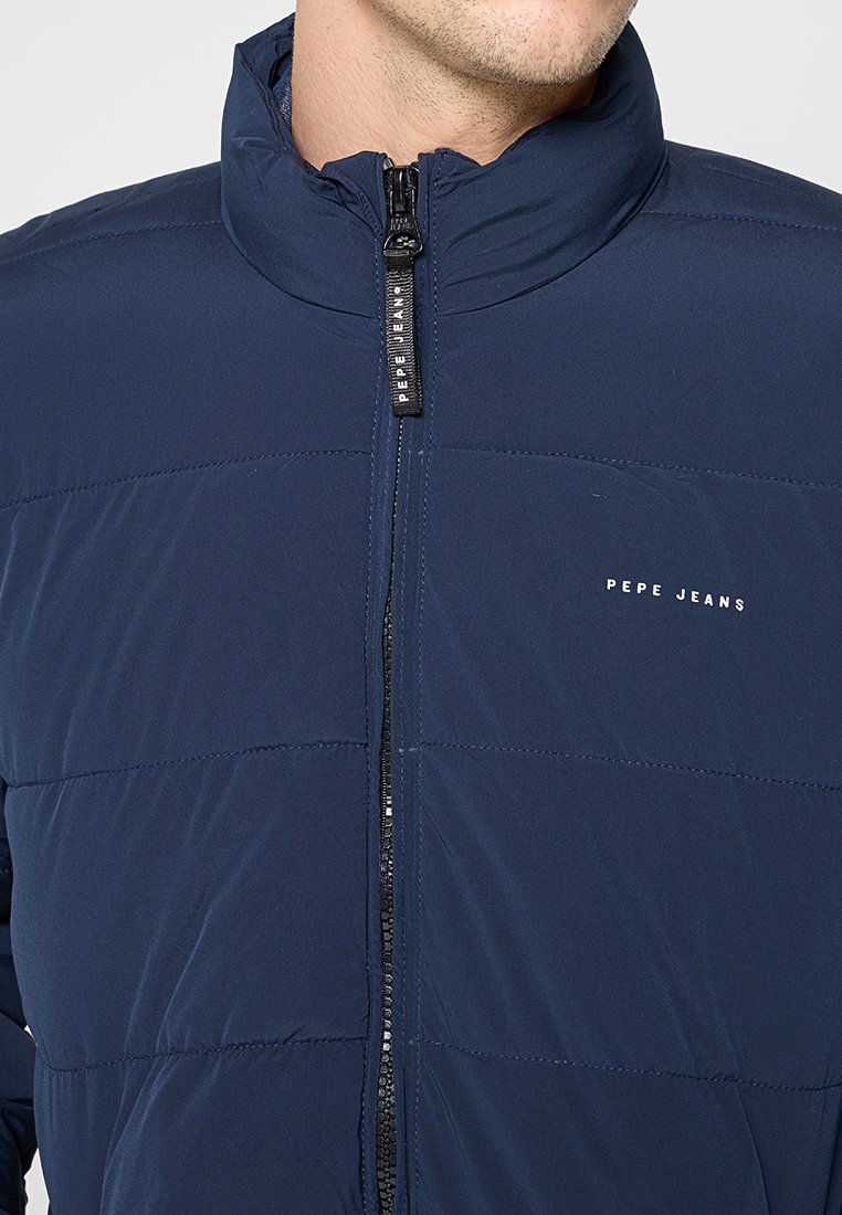 Doudoune bleu marine avec texture matelassée, col haut et fermeture éclair à l'avant. Présente le logo "Pepe Jeans" en blanc sur la poitrine gauche.