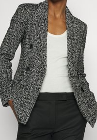 Zwart-witte blazer met structuur, voorzien van een reverskraag, dubbele knoopsluiting en twee voorzakken, gecombineerd met een lichtgevoerde tanktop.