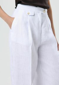 White linen trousers with a high waist, featuring two side pockets, a smooth texture, and two light-colored buttons on the waistband.