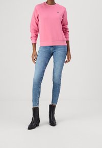 Różowa bawełniana bluza z dzianiny ze ściągaczami, zestawiona z niebieskimi dopasowanymi dżinsami i czarnymi skórzanymi botkami za kostkę. Prosty design, bez wzorów i zdobień.