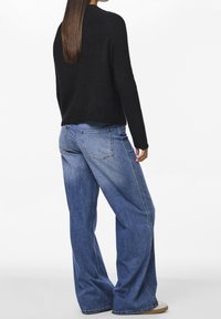 Pull noir en maille avec une silhouette ample, associé à un jean bleu clair à jambes larges. Le jean présente des coutures minimales et deux poches arrière.