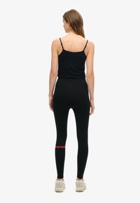 Top nero senza maniche e leggings neri a vita alta con una texture liscia; i leggings presentano una grafica rossa "#SPORTSWEAR" sulla parte inferiore della gamba.