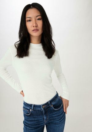 Witte langemouwen top met een hoge hals, gecombineerd met donkerblauwe, slim-fit jeans met vijf pockets en een knoopsluiting.