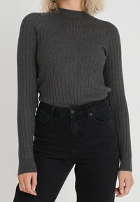 Pull gris côtelé avec un col montant et des manches longues, associé à un jean noir taille haute. Tissu en maille douce avec une texture verticale.