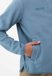 Light blue fleece jacket with a buttoned collar, side pockets, and a textured surface. Features an embroidered logo on the chest.
