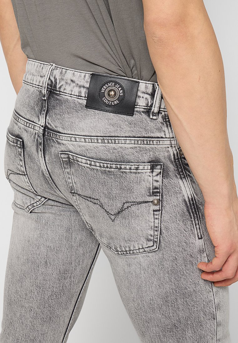 Jeans in denim grigio con una finitura sbiadita e consumata. Presentano un'etichetta nera in vita e due tasche posteriori con dettagli cuciti.