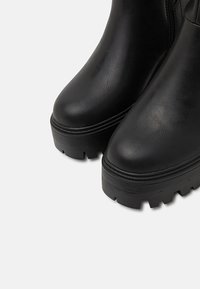 Black ankle boots with a smooth synthetic leather finish, rounded toe, chunky tread sole, and side zipper closure.
