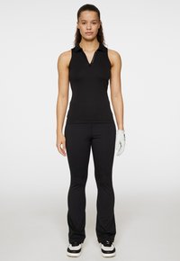 Svart ärmlös pikétröja med dragkedjedetalj vid kragen, matchad med svarta tighta byxor och en vit golfhandske.