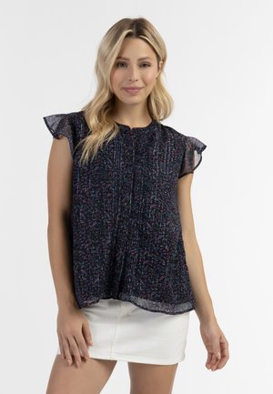 Blusa nera floreale con maniche corte a volant, texture arricciata e motivo multicolore. Abbinata a una gonna bianca.