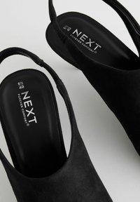 Zapatos slingback de ante negro con puntera redondeada, textura suave, plantilla acolchada y detalles de marca en el interior. Talla 6.5 UK.